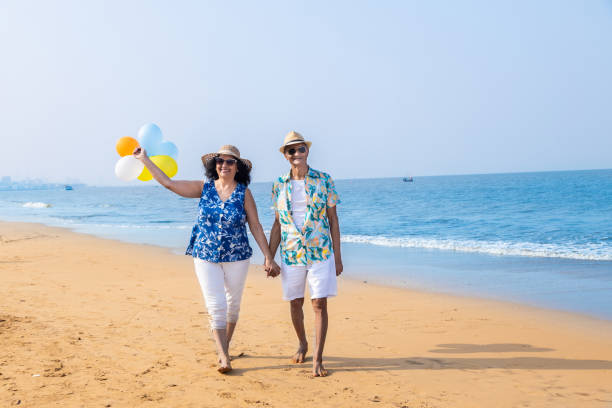 Senior indian couple with colorful balloon in hands walking together at the beach. Enjoying vacation, holiday at beach. Copy space.